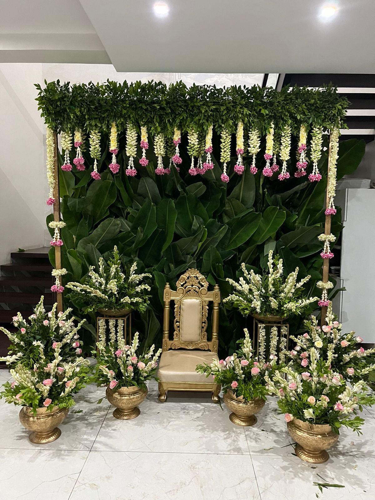 Green leaf backdrop with hanging flowers and gold chair